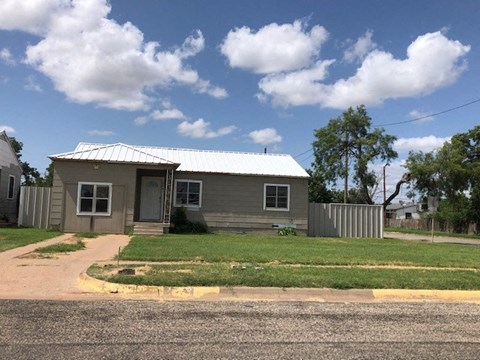 A small house with a grey roof and a grey door is surrounded by a grassy area and a paved driveway.