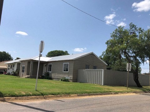 A grey house with a white fence and a tree in front.