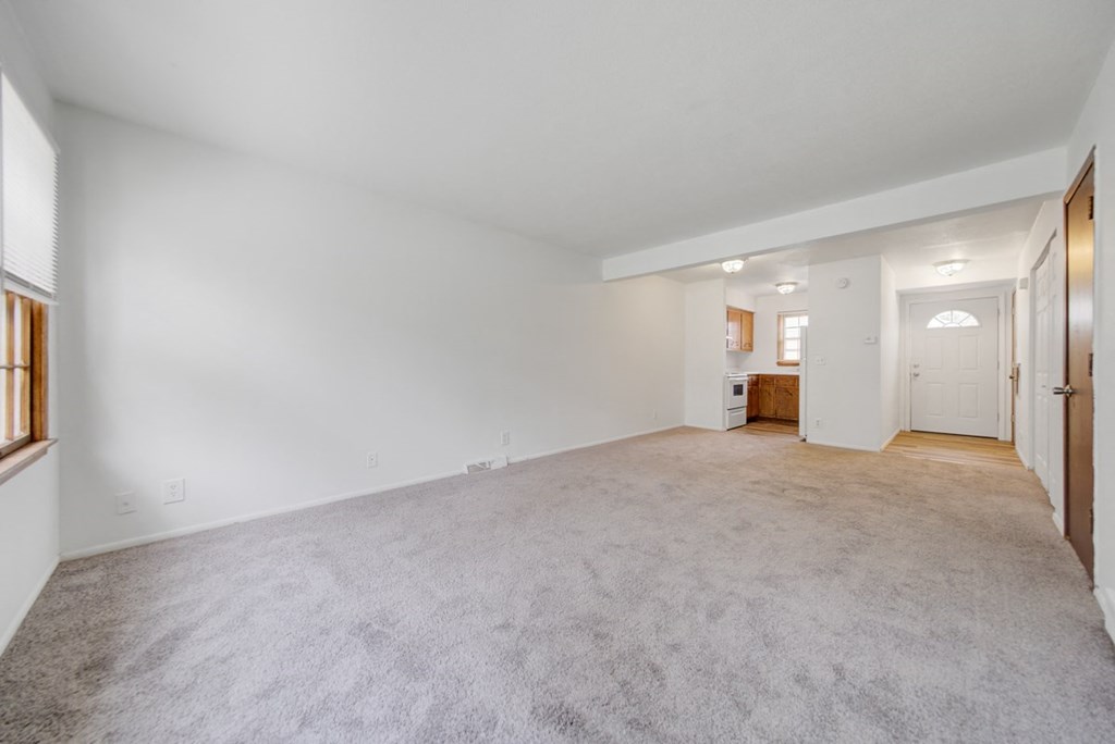 a living room with carpet and a door to a kitchen