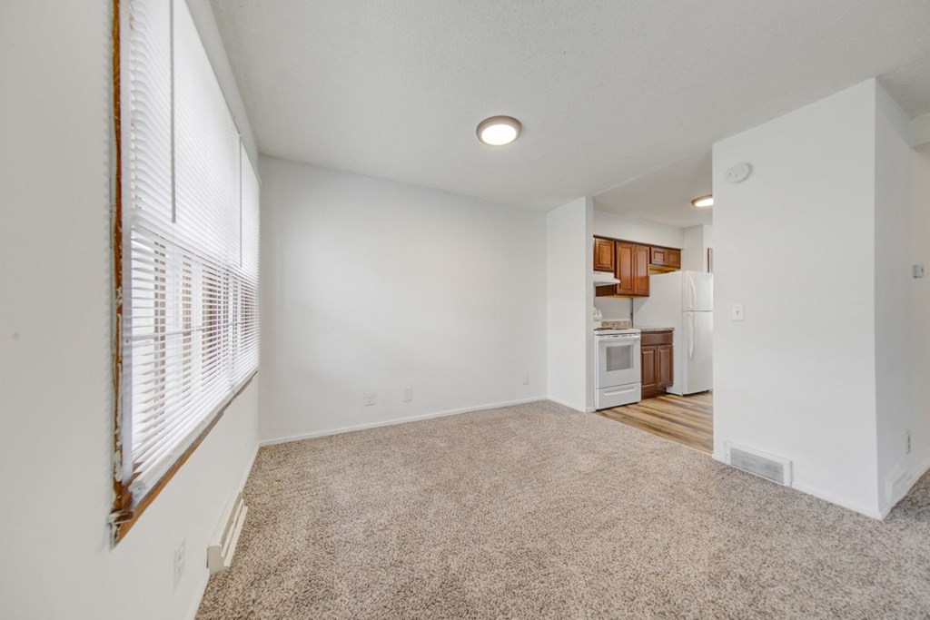 an empty living room with a large window and a kitchen