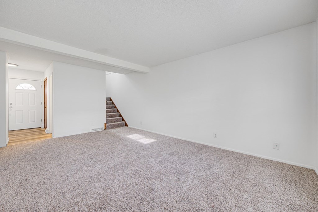 the living room and dining room of a house with white walls and carpet