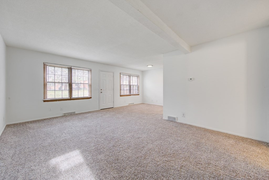 an empty living room with white walls and carpet and a window