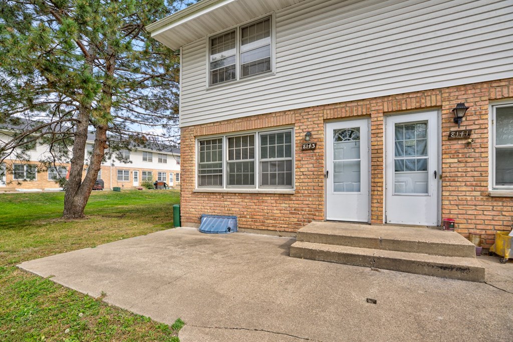 the front door of a brick house with steps and a driveway