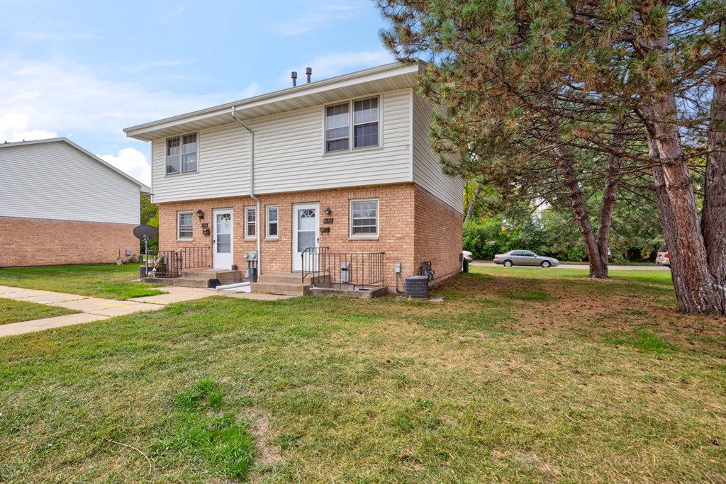 a white and brick house with trees and a sidewalk