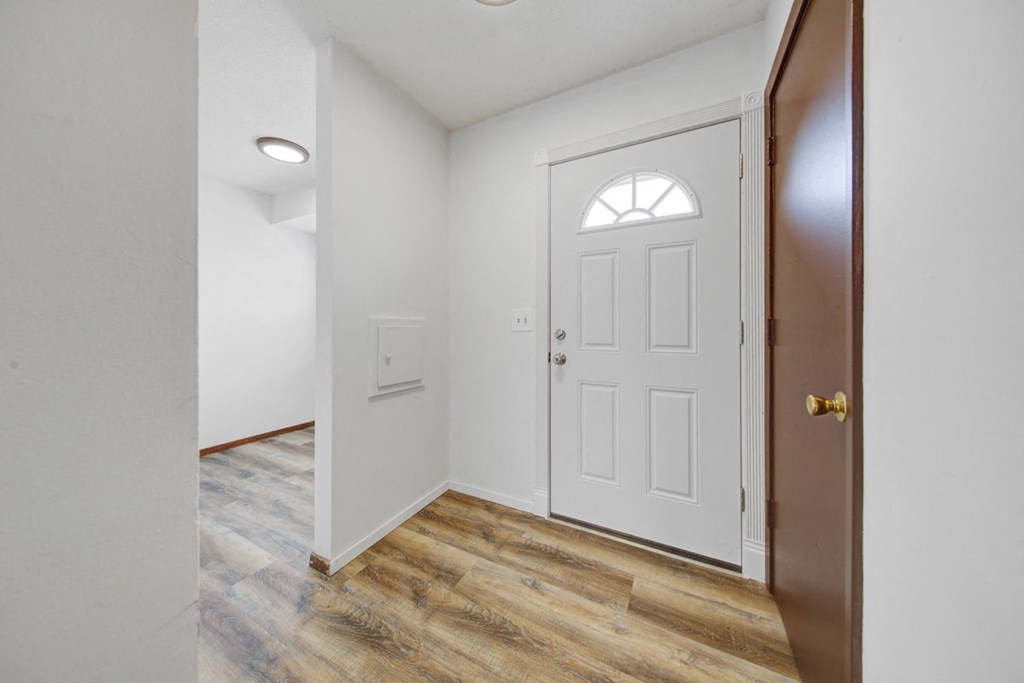 a bedroom with a white door and a hallway with wood flooring