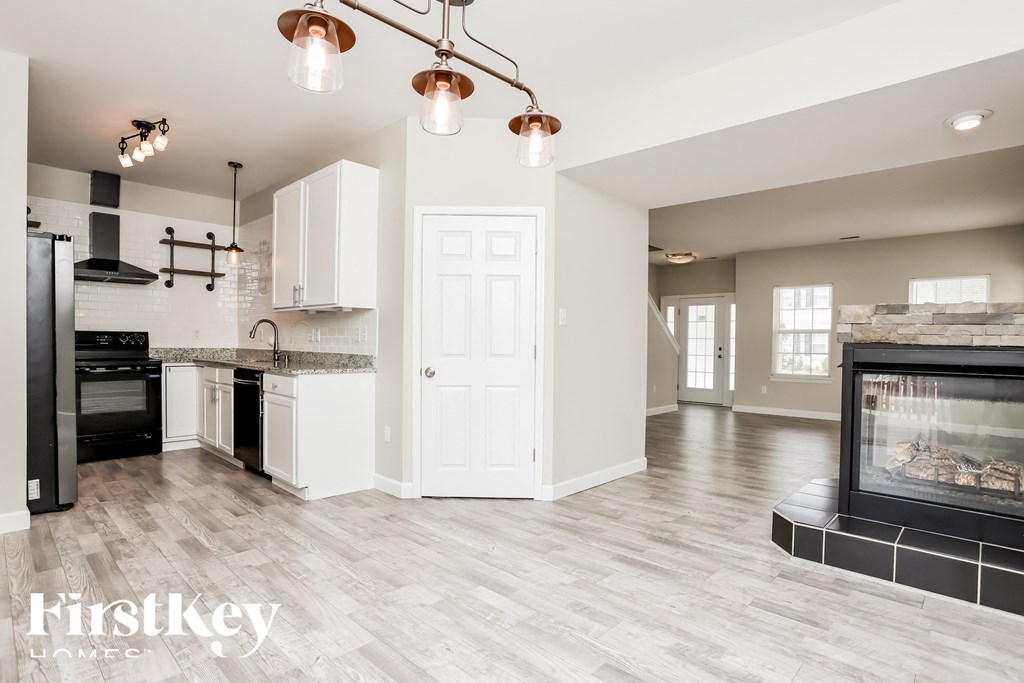A modern kitchen with a black fridge and stove, white cabinets, and a copper chandelier.