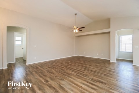 the spacious living room with hardwood flooring and a ceiling fan