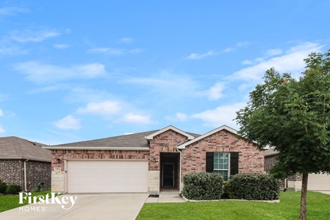 A brick house with a garage door and a tree in front.