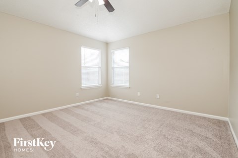 a spacious living room with carpet and two windows