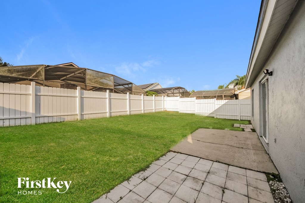 a fenced backyard with a grass lawn and a white fence
