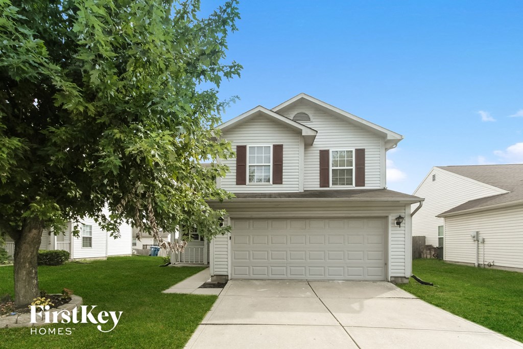 a white house with a driveway and a tree