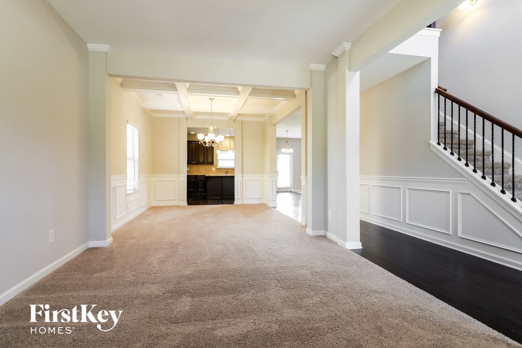 A spacious hallway with a carpeted floor, a staircase with a black railing, and a chandelier hanging from the ceiling.