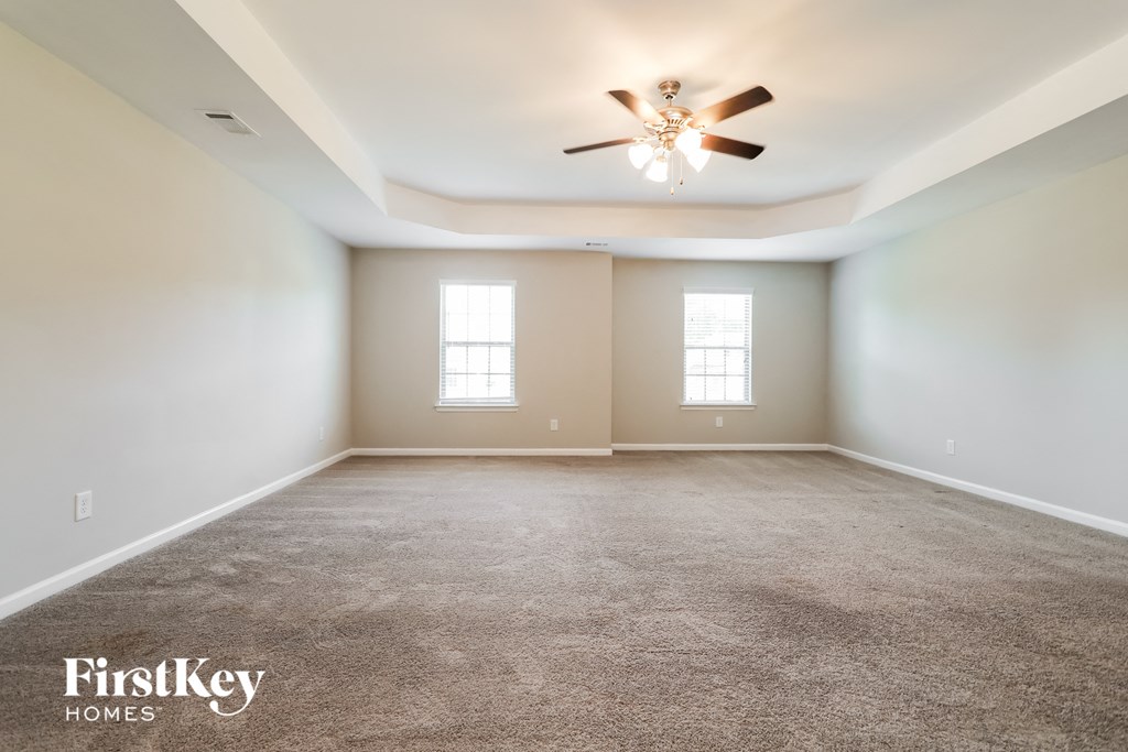 A spacious room with a ceiling fan and two windows.