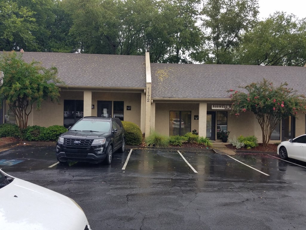 A white car is parked in a parking lot in front of a building.