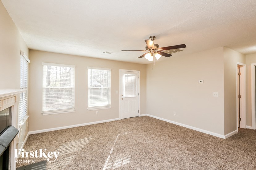 A spacious room with a carpeted floor, a ceiling fan, and a fireplace with a mantelpiece.