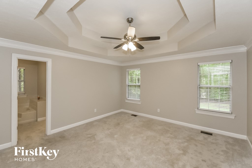 A spacious room with a ceiling fan and two windows.