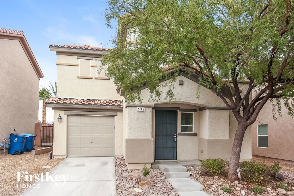 A beige house with a black door and a tree in front.