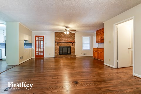 an empty living room with a brick fireplace and wooden floors