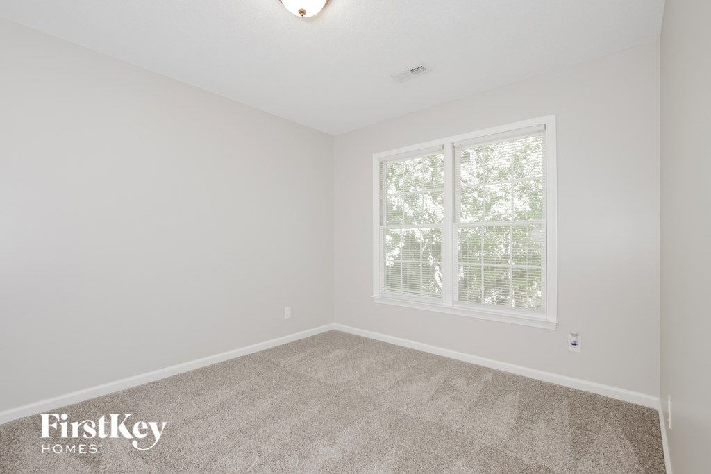 a bedroom with white walls and carpet and a window