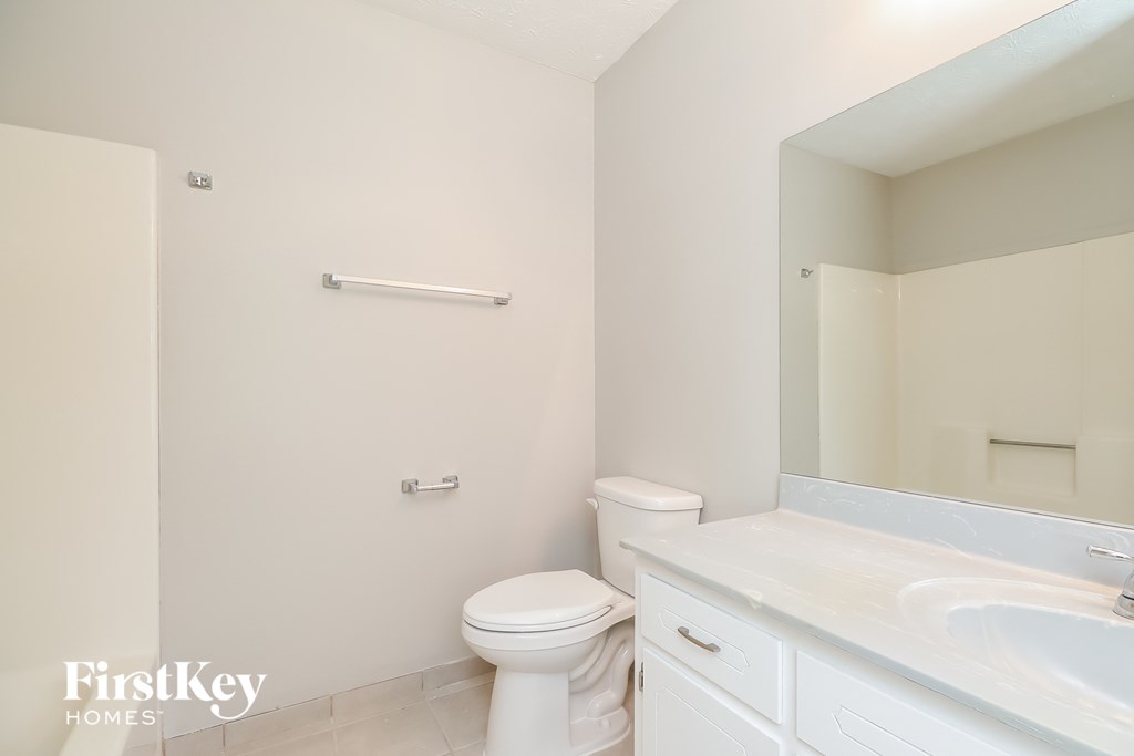 A white toilet sits in a bathroom with a white sink and a white mirror.