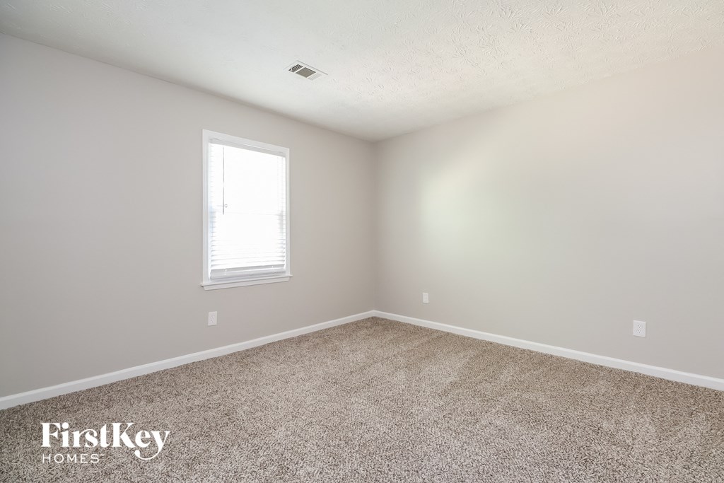 A room with a carpeted floor and a window letting in light.