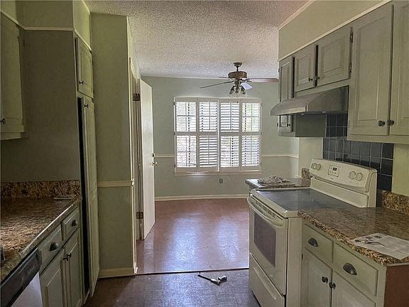 A kitchen with a white stove top oven and a fan on the ceiling.