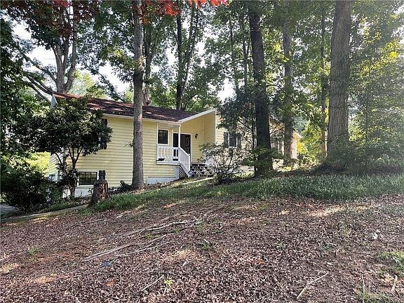 A yellow house is surrounded by trees and leaves on the ground.