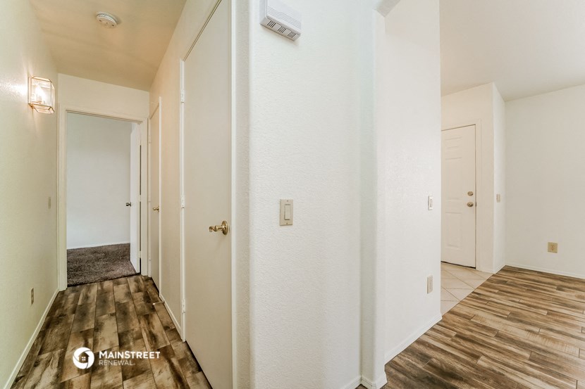 a hallway with white walls and wood flooring and a door