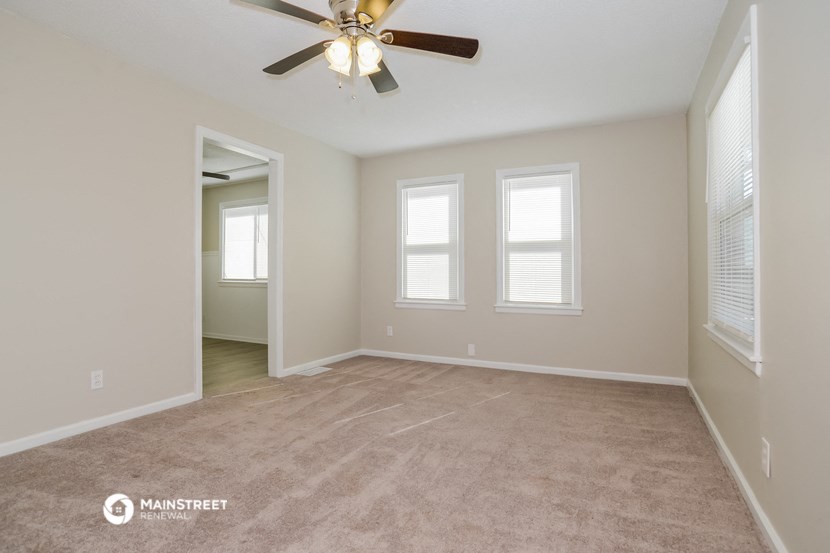 an empty living room with a ceiling fan and three windows