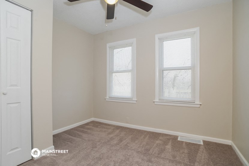 the spacious living room with two windows and a ceiling fan