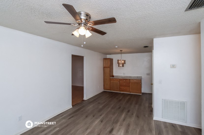 an empty living room with a ceiling fan and a kitchen