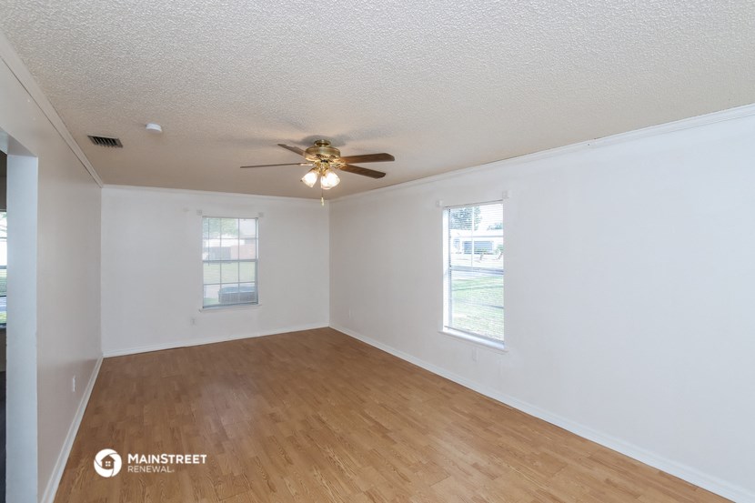 a living room with white walls and a ceiling fan and wood floors