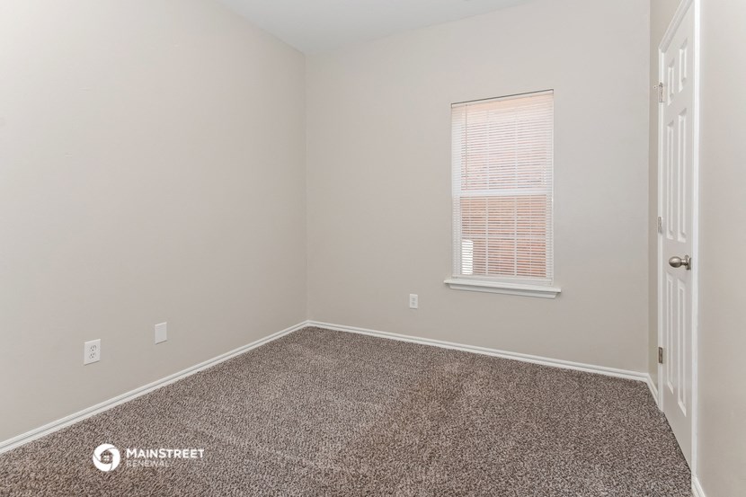 the bedroom of a small house with carpet and a window