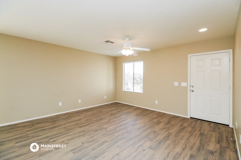 the spacious living room with wood flooring and a ceiling fan