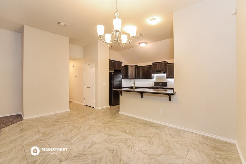 the living room and kitchen of an apartment with a kitchen island and a black refrigerator