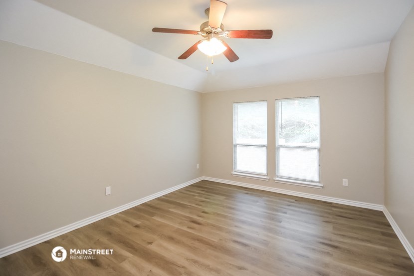 an empty living room with a ceiling fan and two windows