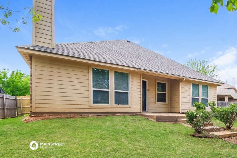 the front of a tan house with a lawn and a backdoor