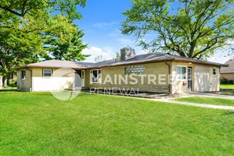 a small tan house with a grass lawn and trees