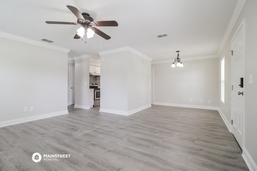 an empty living room with a ceiling fan and a kitchen