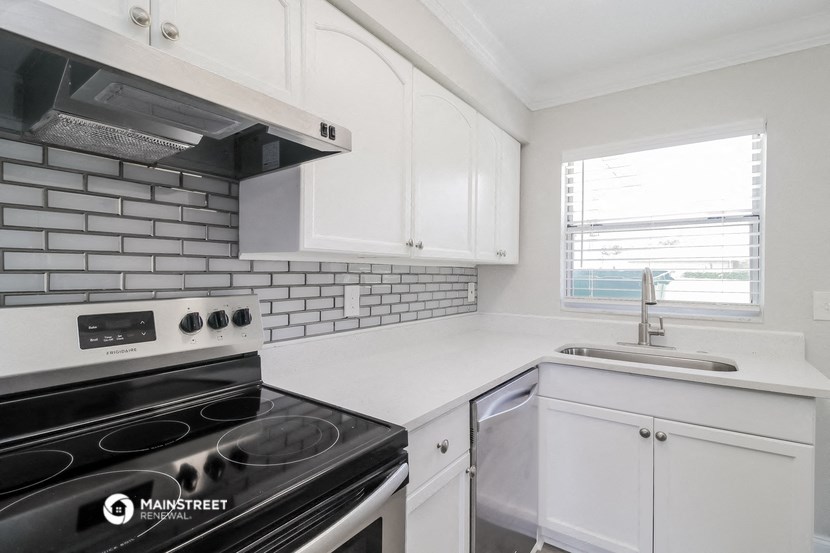 an empty kitchen with white cabinets and appliances and a window