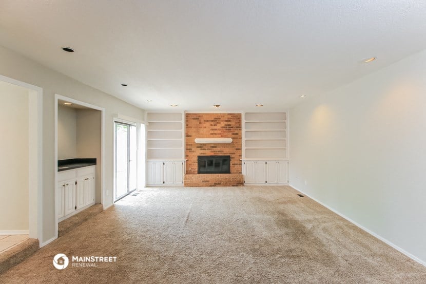 an empty living room with a brick fireplace and white cabinets