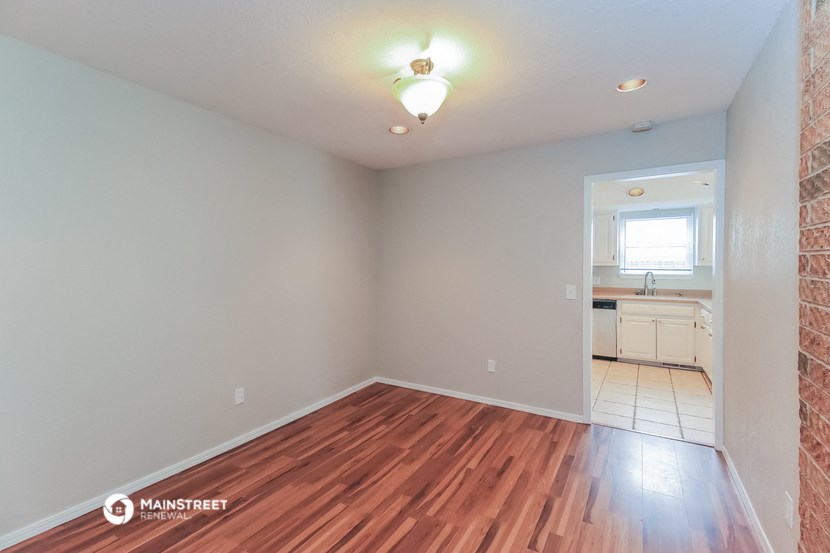 an empty living room with wood flooring and a kitchen
