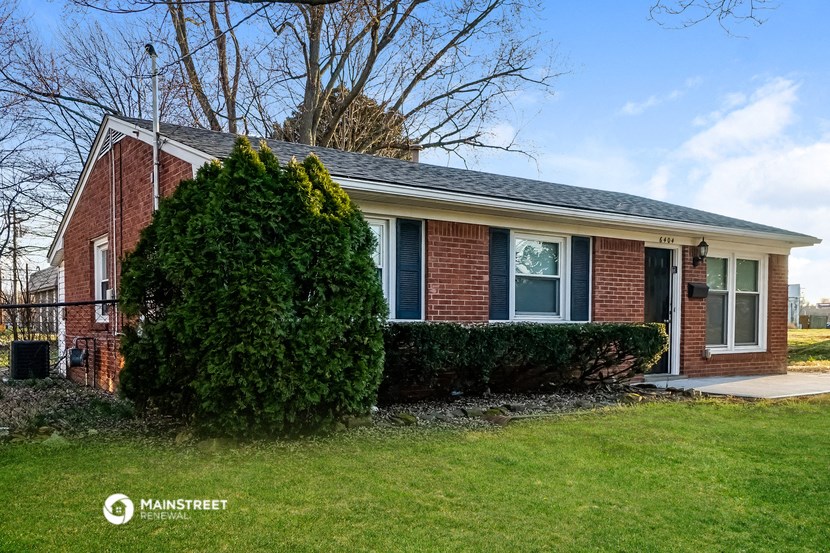 the front of a brick house with a lawn and a tree