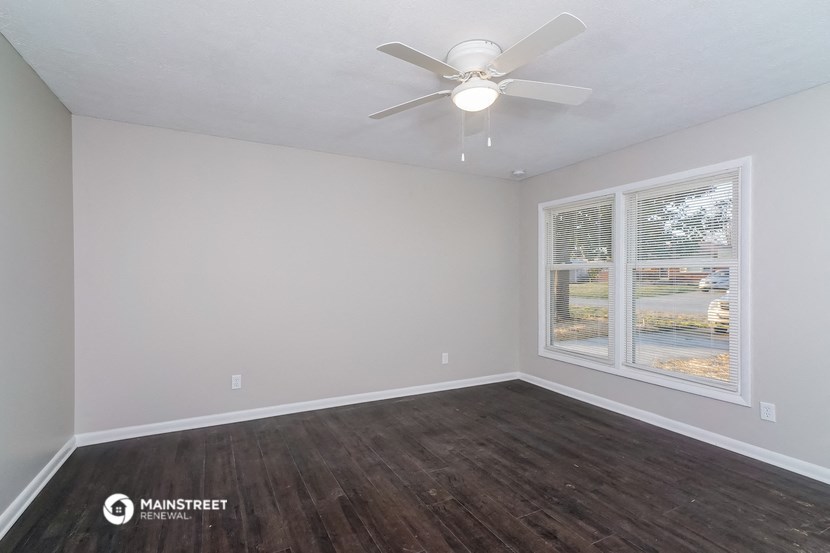 the spacious living room with a large window and a ceiling fan