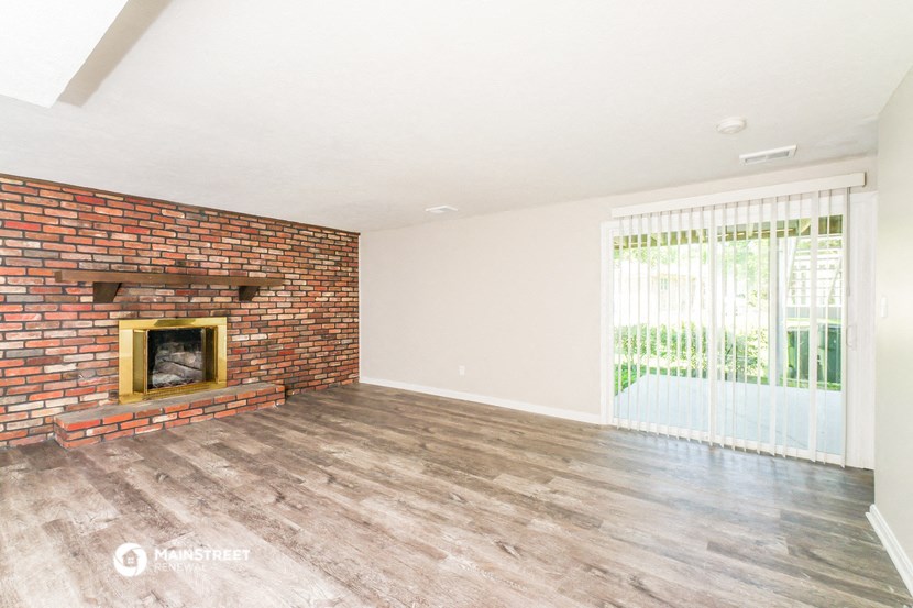 an empty living room with a brick fireplace and a sliding glass door