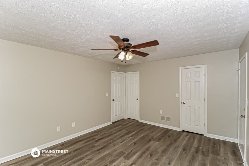 the spacious living room with ceiling fan and doors