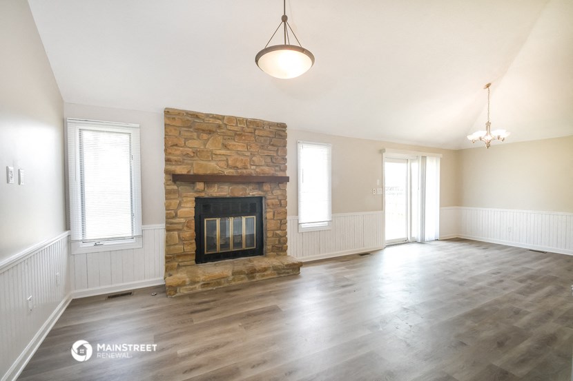 an empty living room with a stone fireplace and wooden floors
