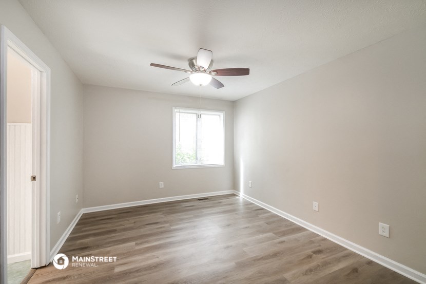the spacious living room with wood flooring and a ceiling fan