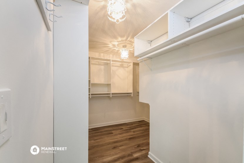 a walk in closet with white walls and wood flooring