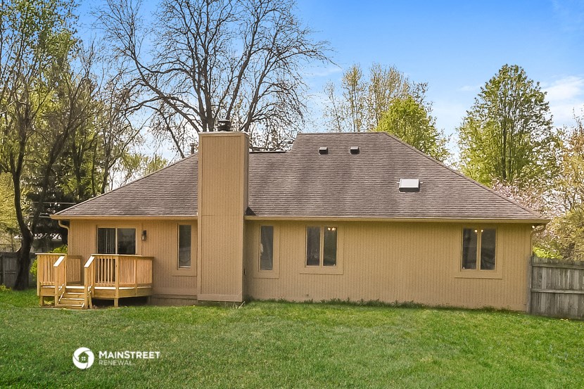 a tan house with a deck and trees in the background